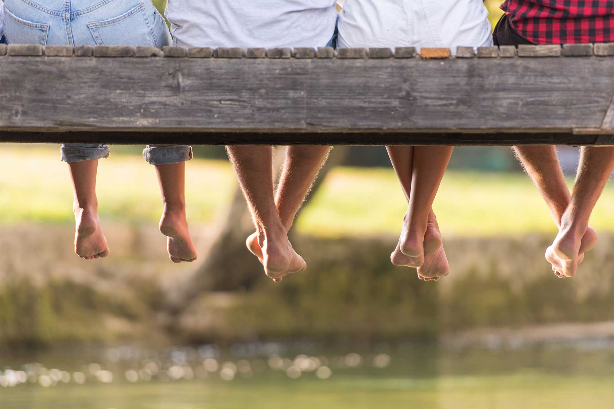 Fyra personer sitter på brygga med benen hängande fritt. Man ser bara underkroppen på personerna.